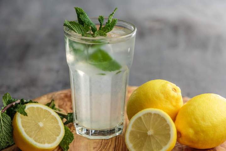 glass of water filled mint leaves and lemon slices surrounded by whole and sliced lemons