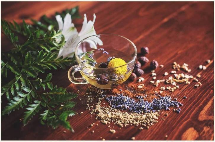 clear teacup filled with water and flowers beside different types of powder placed on a wooden surface