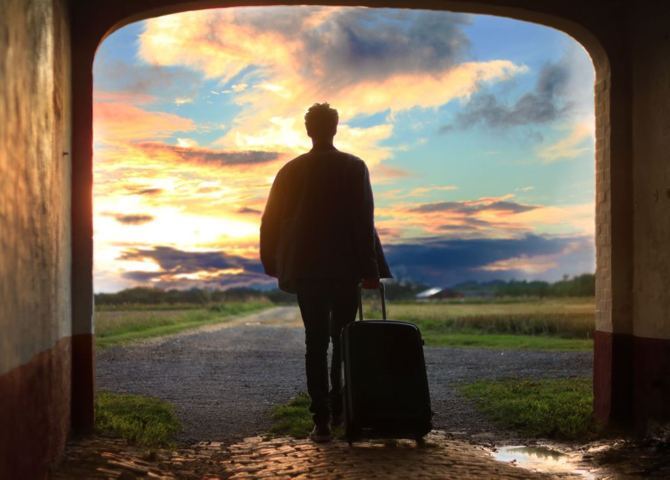 person framed in an entry way silhouette dragging a luggage bag